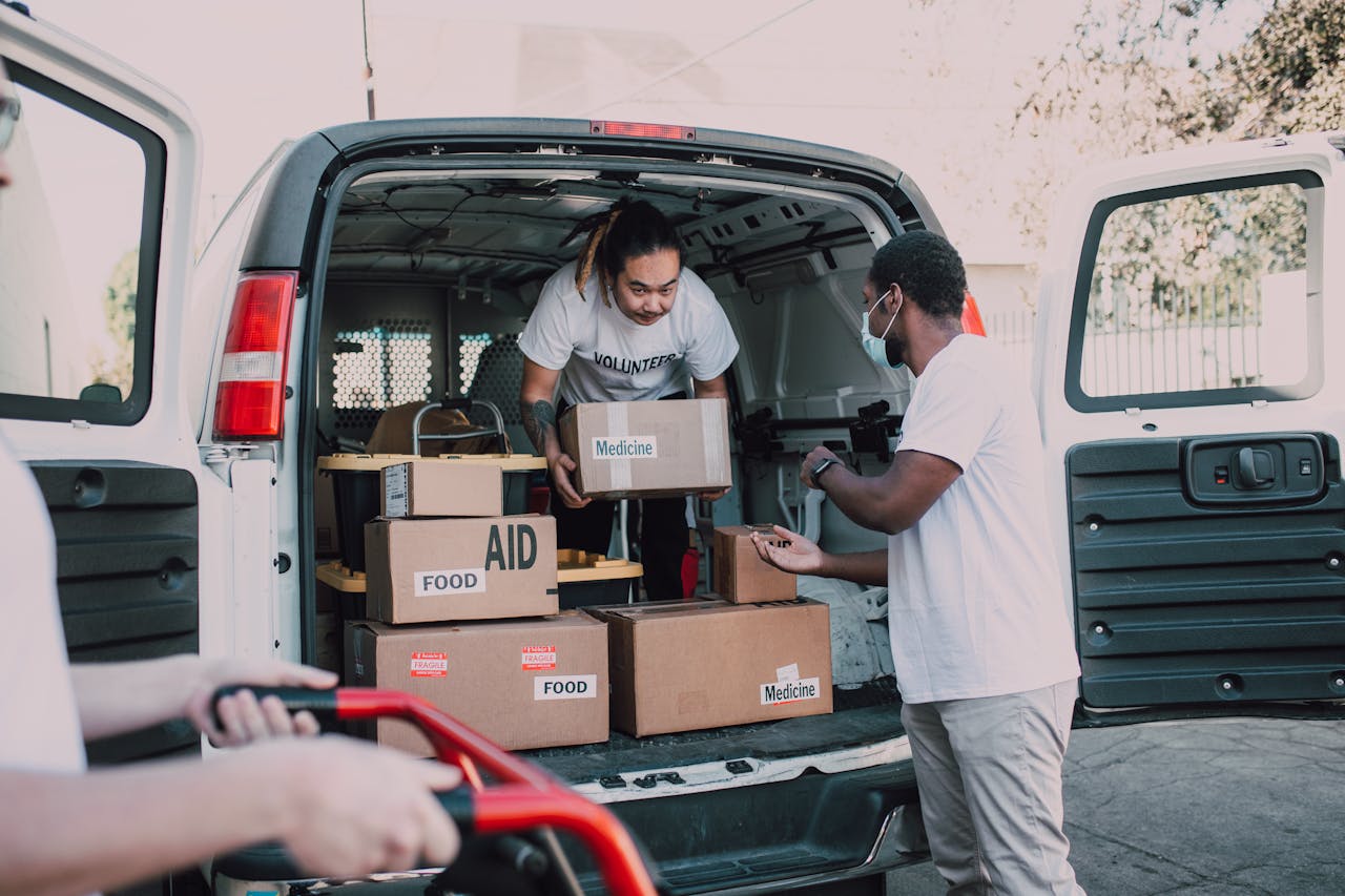 Volunteers unloading boxes labeled food and medicine from a van for charity.